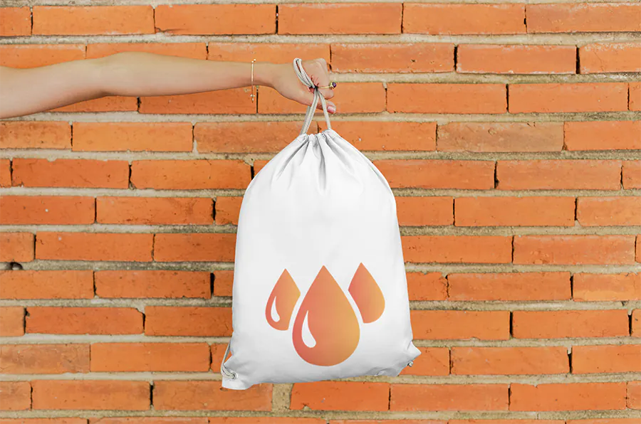 mockup-of-a-hand-holding-a-drawstring-bag-against-a-brick-wall-27574